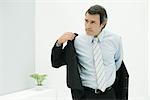 Man in suit putting on jacket, looking away