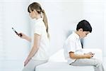Young woman holding cell phone with back turned on boy playing handheld video game