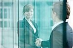 Businesswoman and businessman meet and shake hands at building entrance