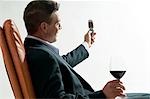 Jeune homme en costume/tailleur assis avec verre de vin rouge et le téléphone mobile