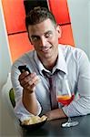 Jeune homme assis avec un verre de vin orange et téléphone mobile