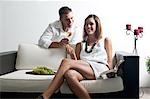 Young man leaning on couch with white wine and young woman reading book and eating grapes