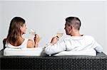 View of couple from the back sitting on couch drinking white wine