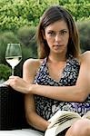 Young woman sitting on couch in vineyard with white wine and a book