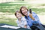 Mère et fils assis dans le parc à l'aide de téléphone portable pour prendre une photo d'eux-mêmes