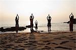 Women practicing yoga on beach at sunset