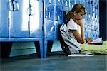 Female junior high student sitting on hall floor leaning against lockers reading book