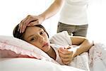 Girl checking temperature with thermometer, mother caressing forehead