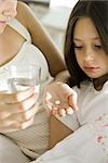 Mother giving medicine to take with glass of water to ill daughter