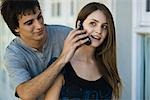 Young man holding cell phone to girlfriend's ear