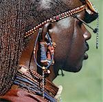 Detail eines Massai-Kriegers Ohr Ornamente und andere Perlen oder Metall Verzierungen. Die Maasai-Praxis der durchdringenden Ohren in der Adoleszenz und die Lappen nach und nach zu dehnen ist allmählich Aussterben. Diese Krieger Körper und seine lange Zöpfe haben mit Roter Ocker mit Tierfett gemischt beschmiert worden.