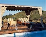 Sun loungers on a canopied deck beside the swimming pool at Uplands Homestead