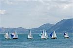 Wales,Anglesey,Beaumaris. Dinghies race during a regatta on the Menai Straits against the backdrop of the Snowdonia Mountains.