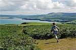 UK, Wales in Pembrokeshire. Ein Junge verläuft entlang dem Pembrokeshire Küstenweg auf Dinas Kopf mit Blick auf den Newport Bay jenseits.