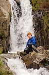 Pays de Galles, Conwy, Snowdonia. Un jeune garçon assis à côté d'une cascade dans Idwal MCG au pied de la Glyders