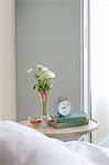 Bedside table with cut flower and alarm clock