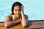 Woman in water resting at edge of swimming pool, portrait