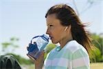 Woman listening to earphones outdoors, drinking water from bottle