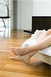 Woman's bare feet and legs dangling off end of bed
