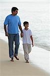 Father and son holding hands and walking down the beach.