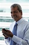 Head shot of mature Indian man holding hand phone