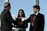 Business men shaking hands while female colleague looks on.