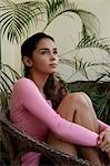 Young woman sitting on chair holding knees and looking up