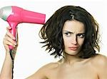 Young woman using hairdryer, frowning