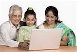 Girl using a laptop with her grandparents and smiling