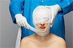 Surgeon wrapping bandage on woman's face