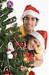 Portrait of a couple peeking through a Christmas tree and smiling
