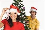 Frau zeigen eine Zuckerstange mit einem Mann dekorieren einen Weihnachtsbaum im Hintergrund