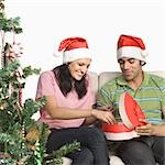Couple sitting on a couch and unpacking a Christmas present