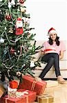 Femme assise sur un canapé près d'un arbre de Noël et souriant