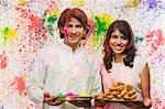 Couple holding plates of powder paints and gujiyas