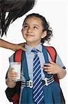 Schoolgirl holding a glass of milk and looking at her mother