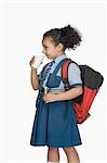 Schoolgirl drinking a glass of milk and carrying a schoolbag