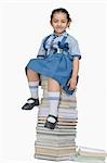 Schoolgirl sitting on a stack of books and smiling