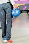 Junger Mann hält eine Bowling-Kugel in eine Bowlingbahn