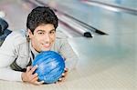 Young man lying with a bowling ball in a bowling alley