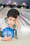 Young man lying with a bowling ball in a bowling alley