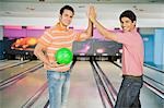 Deux jeunes hommes High-Five dans une ruelle de bowling