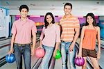 Two young couples holding bowling balls in a bowling alley