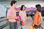 Young couple with their friend holding bowling balls in a bowling alley