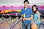 Junges Paar mit einer Bowling-Kugel und eine Trophäe in eine Bowlingbahn