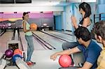 Young woman holding a bowling ball and her friends encouraging her