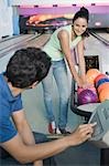 Young man operating the control panel and his friend looking at him in a bowling alley