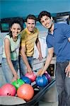 Zwei junge Männer und eine junge Frau in eine Bowlingbahn Bowling-Kugeln halten