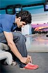 Side profile of a young man tying his shoelace in a bowling alley