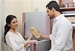 Femme donnant une bouteille d'eau à un homme devant un réfrigérateur